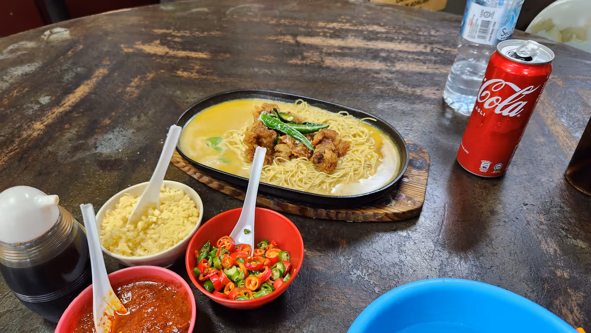 A buttermilk noodle with fried chicken with condiments and a can of soda pop at the right.