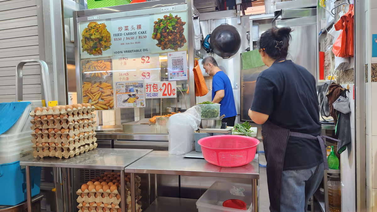 A food stall with tray of eggs and a plastic pink stainer. A woman stands in front of the stall.