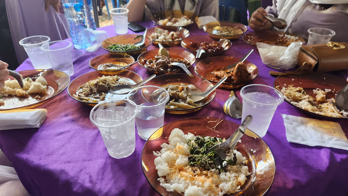 Dishes of food on a round table. There are plastic cups and plates.