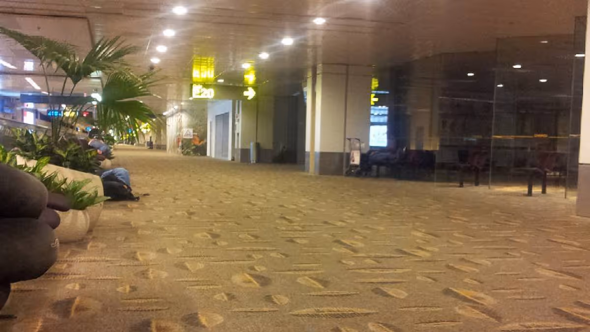 A waiting area with brown carpet. People sleeps on the left side. There is a big yellow arrow pointing to E20 gate.