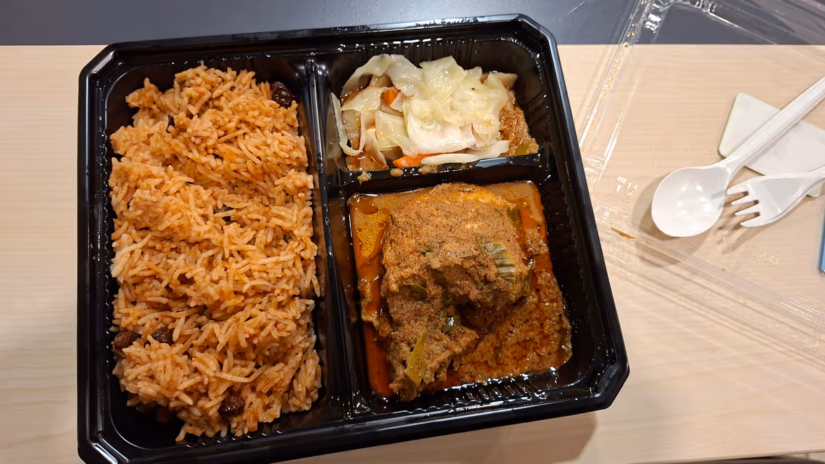 Nasi biryani with vegetables and curry chicken in a lunch box, with utensils on the right