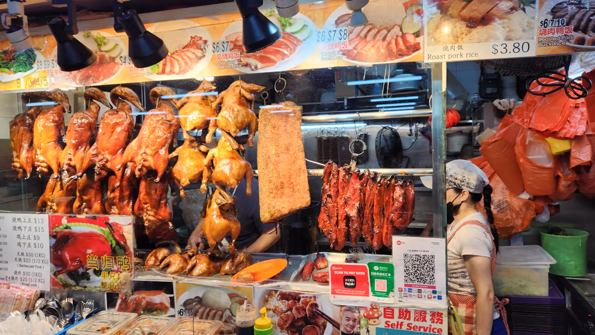 A glass container of food stall with a hanging duck, a chicken and pork.