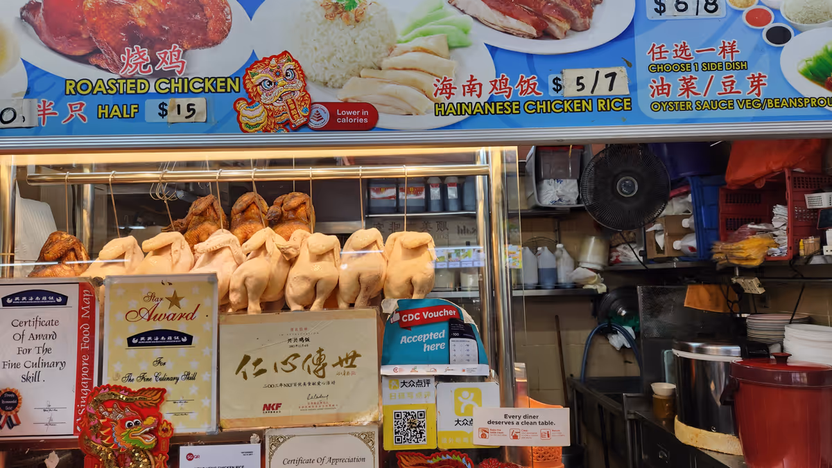 A chicken rice stall with a hanging boil chicket and roast chicken in a glass container.