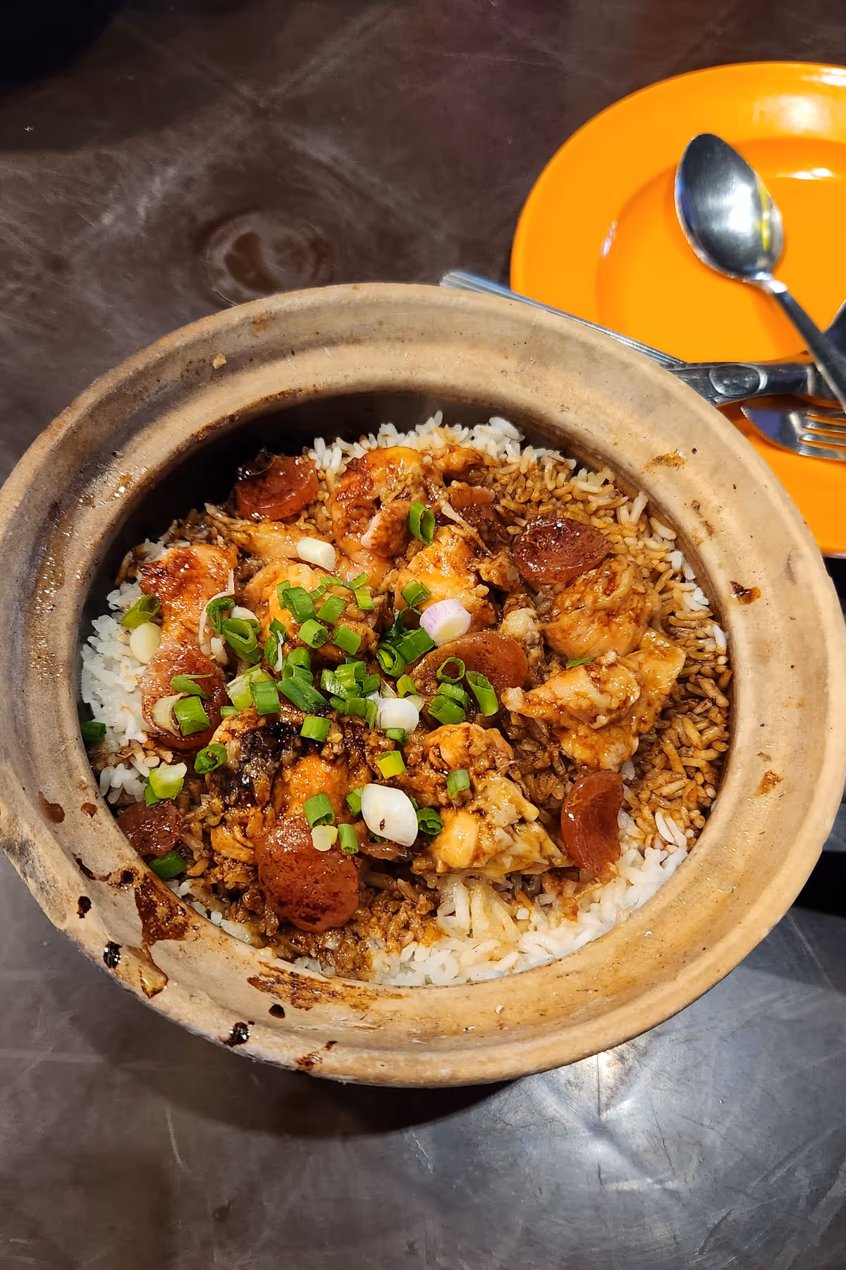 A chicken rice in a clay pot with a slice of Chinese sausage and a spring onion