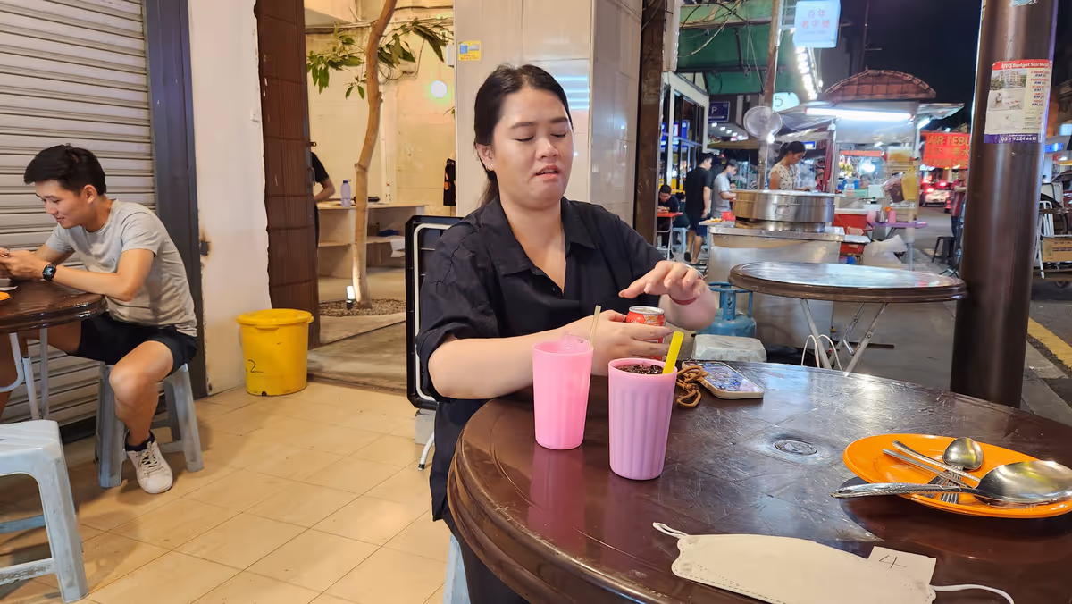A woman opens a soda pop with 2 pink glasses on the wooden table