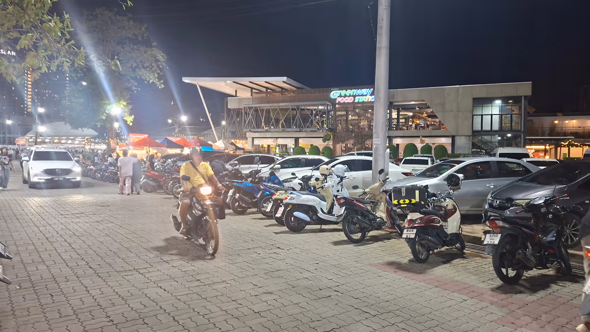 People ride a motorcycle. There are cars parking behind.