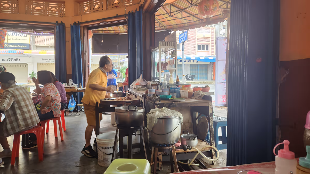 A man is cooking a food. There are big pots. The customers are sitting behind a man.
