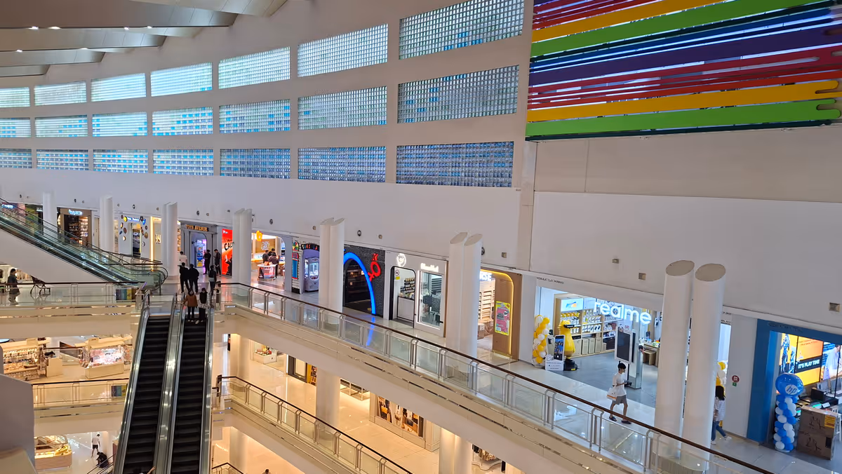 A stained glass window facade inside a shopping mall with natural light, with two elevators on the left and a store next to them