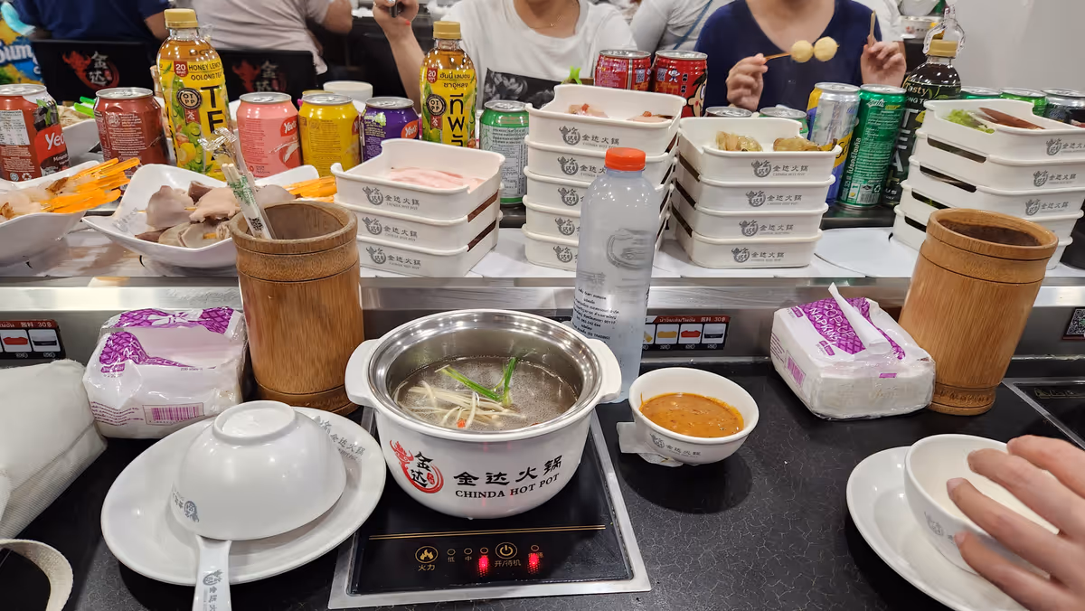 An electric hot pot with raw food and soda pop on the table.