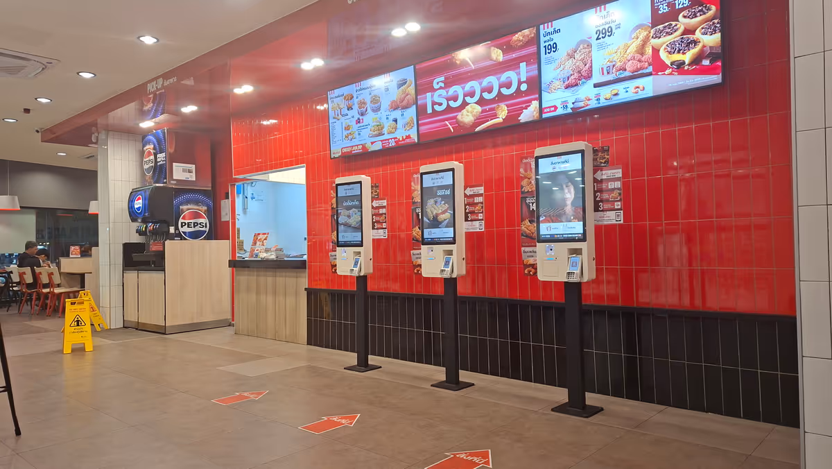 KFC kiosk with an electronic display in front of a red wall.