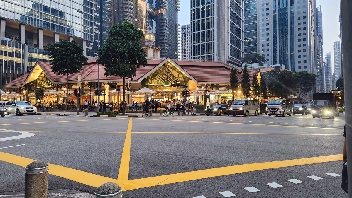 A crosroad junction with a yellow line on the road and a 2 storey building and high rises.
