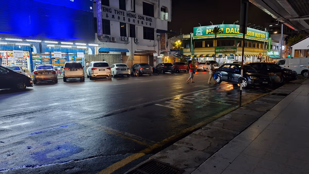 A wet road at night with cars parked along the side, lit by blue signage from a nearby building