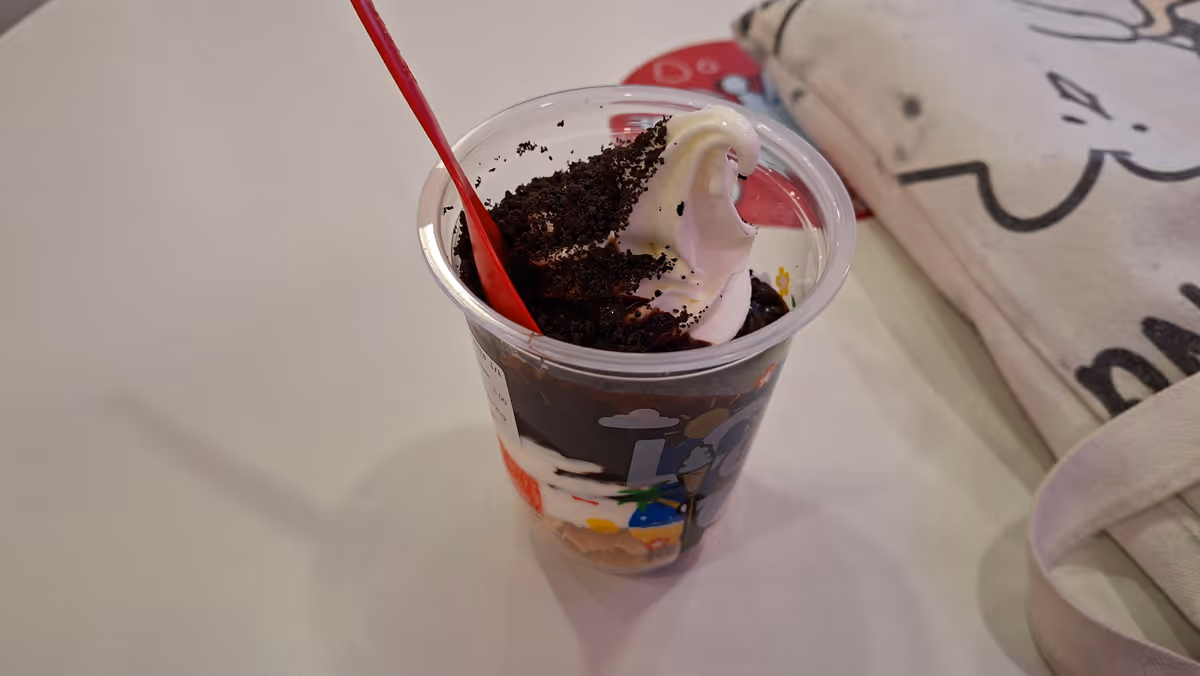 A white sundae in a cup topped with crushed Oreo powder, served with a red spoon