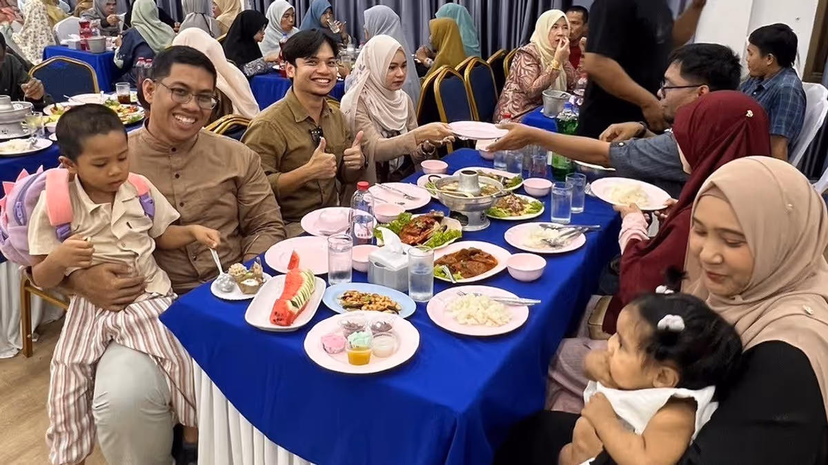 Men smiling with and a woman holding a baby. They are sitting on a table eating food.