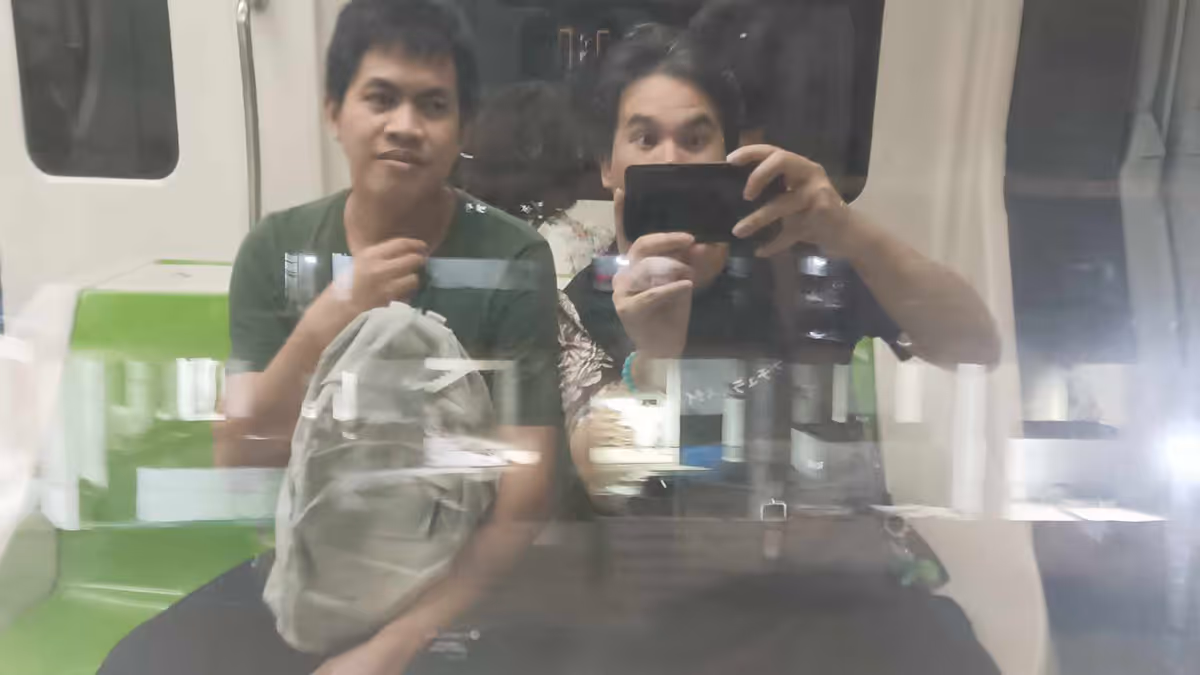 2 men sitting and taking a photo of their reflextion from a windowpane.
