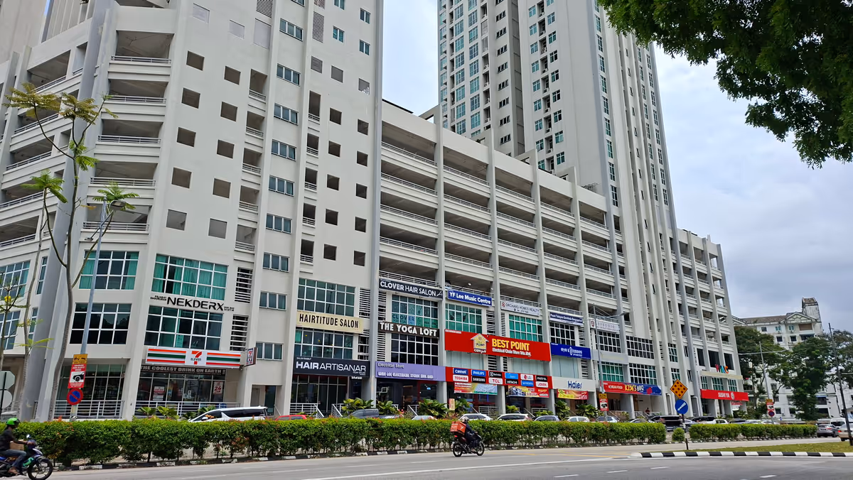 Modern high-rise residential building with ground-floor shops, including a convenience store, along a roadside with light traffic
