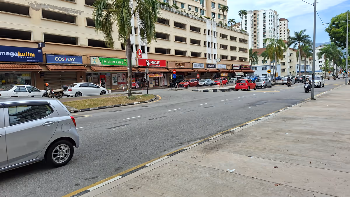 A road with parked cars, with shoplots in the background