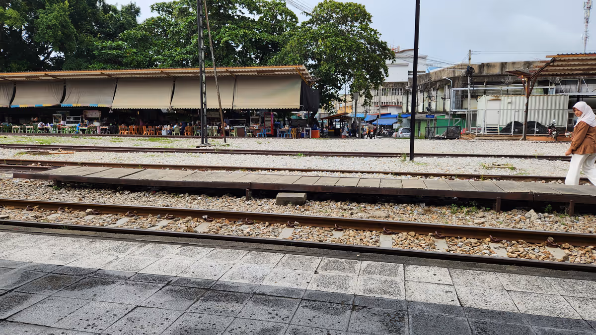 Train tracks and a woman crossing the track. There are shop lots behind.