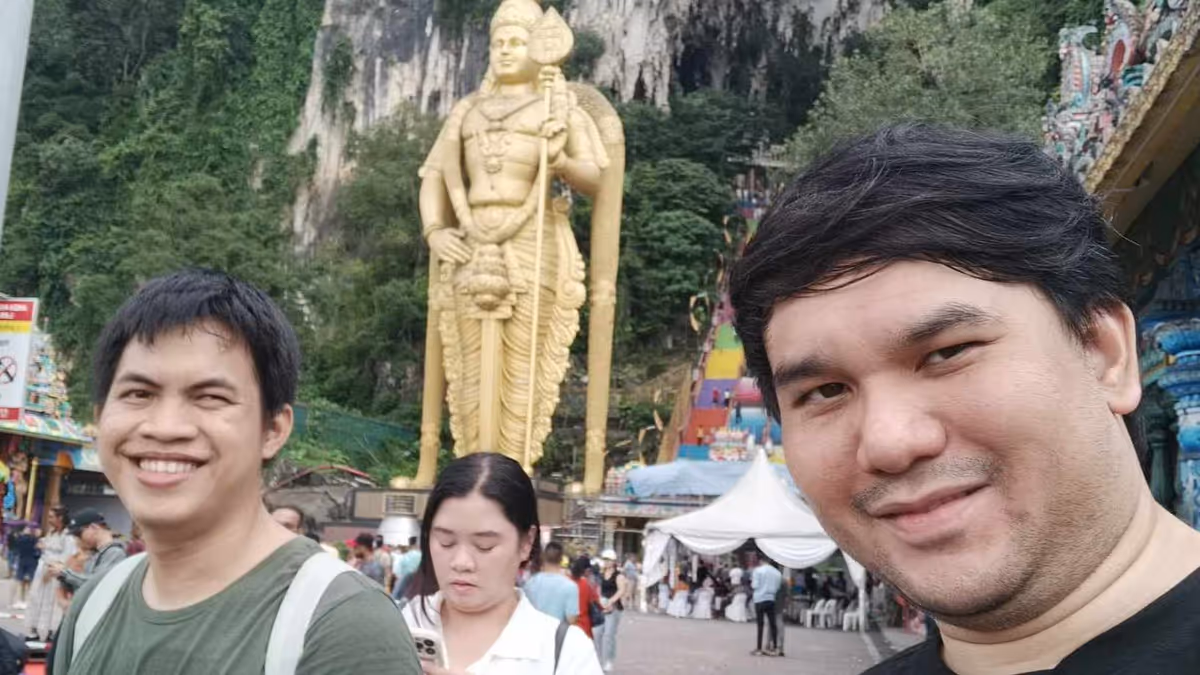 A selfie of 3 people in front of a golden Kartikeya statue
