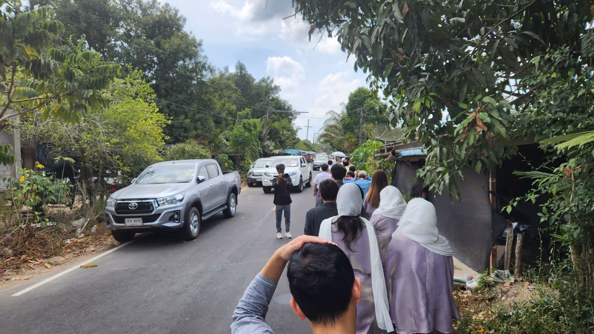People walk along the road with cars on the left side.